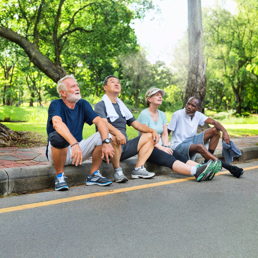Four people sitting on a curb in a park with trees and grass in the background