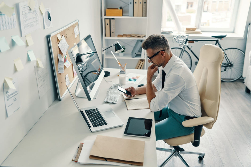 Man sitting at a desk with multiple electronic devices in a modern office setting.