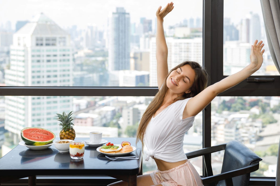 Woman stretching in a room with a cityscape view, enjoying a healthy breakfast.